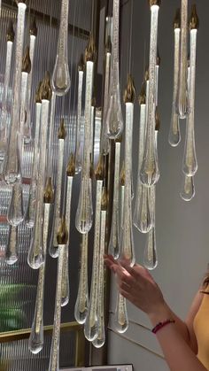 a woman standing in front of a chandelier made out of glass bottles and hanging from the ceiling