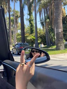 a woman's hand sticking out the window of a car with palm trees in the background