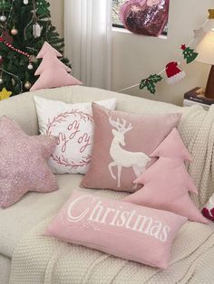 pink christmas pillows on a white couch in front of a christmas tree with lights and decorations