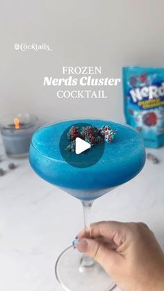 someone is holding up a frozen nerds clusterer cocktail in a wine glass with blue liquid and sprinkles on the rim