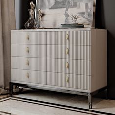 a white dresser with gold knobs and a painting on it's sideboard