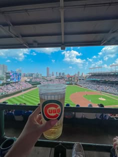 a person holding up a glass with a beer in it at a baseball game on a sunny day