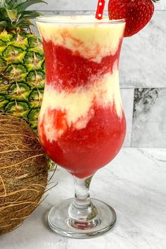 a red and white drink in a glass next to a pineapple