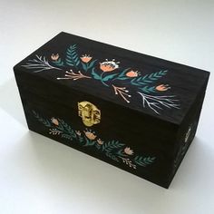 an ornate wooden box with painted flowers and leaves on it's lid, sitting on a white surface