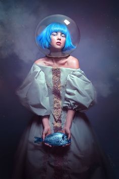 a woman with blue hair wearing a dress and holding a fish in it's mouth