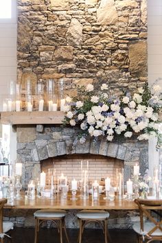 a table with candles and flowers on it in front of a stone fireplace surrounded by chairs