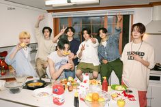 a group of young people standing around a kitchen counter with food and drinks on it