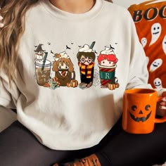 a woman wearing a harry potter sweatshirt holding a coffee mug with three different characters on it