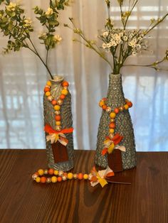 two vases with flowers in them on a table next to a beaded necklace