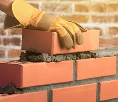 a person wearing yellow gloves is placing bricks into a brick wall