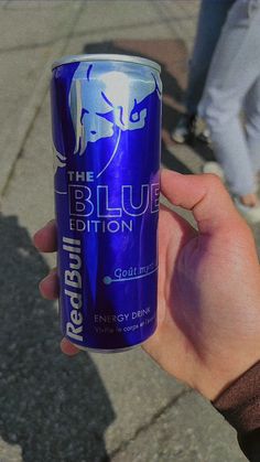 a person holding up a can of red bull blue edition energy drink on the street