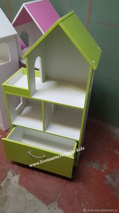 a green and white doll house on display in front of a pink and white wall