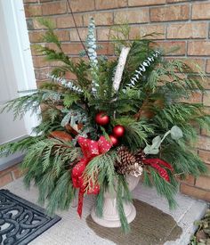 a potted plant with evergreen, pine cones and red ornaments on the front porch