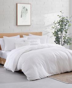 a bed with white comforters and pillows in a room next to a potted plant