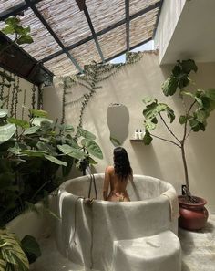 a woman is sitting in an outdoor bathtub surrounded by greenery and potted plants