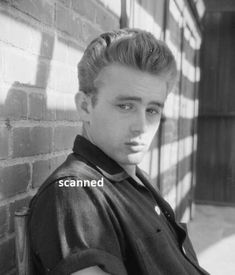 a young man leaning against a brick wall with his arm around the back of his shoulder