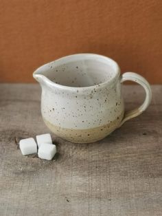 a white cup sitting on top of a wooden table next to small pieces of sugar