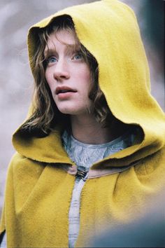 a woman wearing a yellow hoodie and looking at something in front of her face