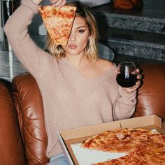 a woman sitting on a couch holding up a slice of pizza in front of her face