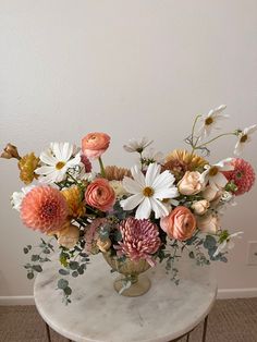 a vase filled with lots of flowers on top of a marble topped table next to a white wall