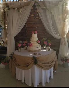 a wedding cake sitting on top of a table covered in white drapes and flowers