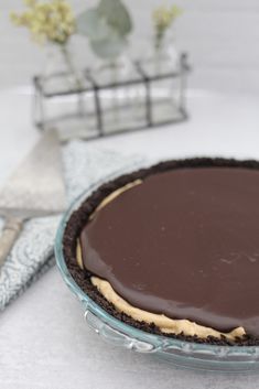 there is a chocolate pie on the table next to a fork and napkin with a vase in the background