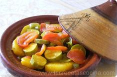 a bowl filled with pickles and carrots next to a wooden hat