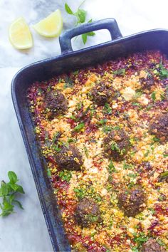 a casserole dish with meatballs and vegetables in it on a marble surface