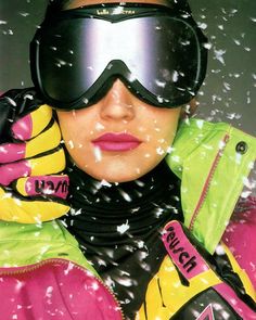 a woman wearing ski goggles and gloves with snow falling all around her, in front of the camera