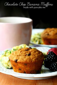 a muffin on a plate next to some berries and a cup of coffee with another muffin in the background