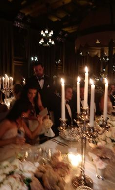 a group of people sitting around a dinner table with candles in the middle of it