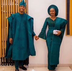 two people standing next to each other wearing green outfits and holding hands in front of a wall