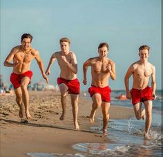 four men running on the beach in red trunks