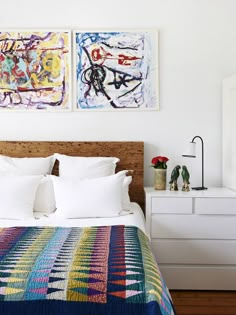 two paintings on the wall above a bed in a room with white walls and wooden headboard