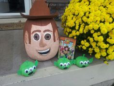 a fake pumpkin with two green googly eyes next to some plants and yellow flowers