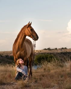 a woman kneeling down next to a brown horse