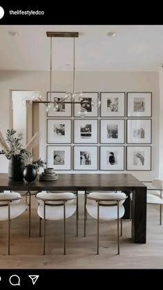 a dining room table with white chairs and pictures on the wall behind it, all in black and white