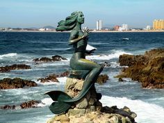 a mermaid statue sitting on top of a rock next to the ocean