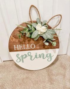 a wooden sign that says hello spring with white flowers and greenery hanging from it