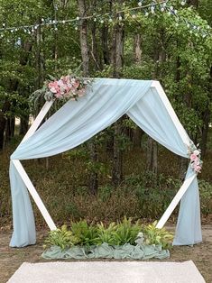 an outdoor wedding ceremony setup with blue drapes and pink flowers on the altar, surrounded by greenery