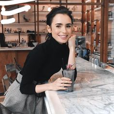 a woman sitting at a bar with a drink in her hand and looking into the camera