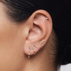 a woman wearing three different types of ear piercings on her left ear and the other one is gold