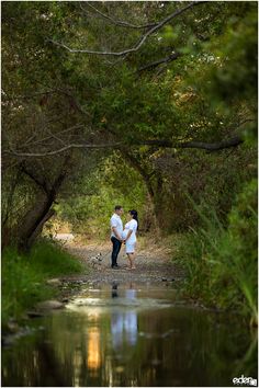 two people standing in the middle of a forest holding hands and looking at each other