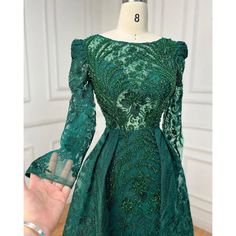 a green dress on a mannequin stand in front of a white wall with a hand holding it