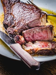 a piece of meat on a plate with a knife and fork next to the steak