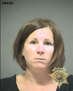 the woman is wearing a police badge and posing for a mug shot in front of a gray wall