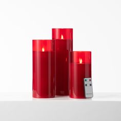 three red candles sitting next to each other with a remote control in front of them