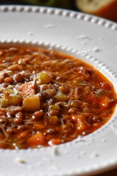 a white plate topped with chili and meat soup next to an orange slice of bread