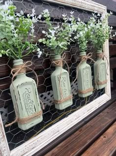 four mason jars with flowers in them are hung on a chicken wire frame, along with twine string