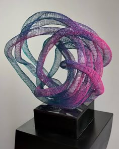 a sculpture is shown on top of a black stand with purple and blue yarn wrapped around it